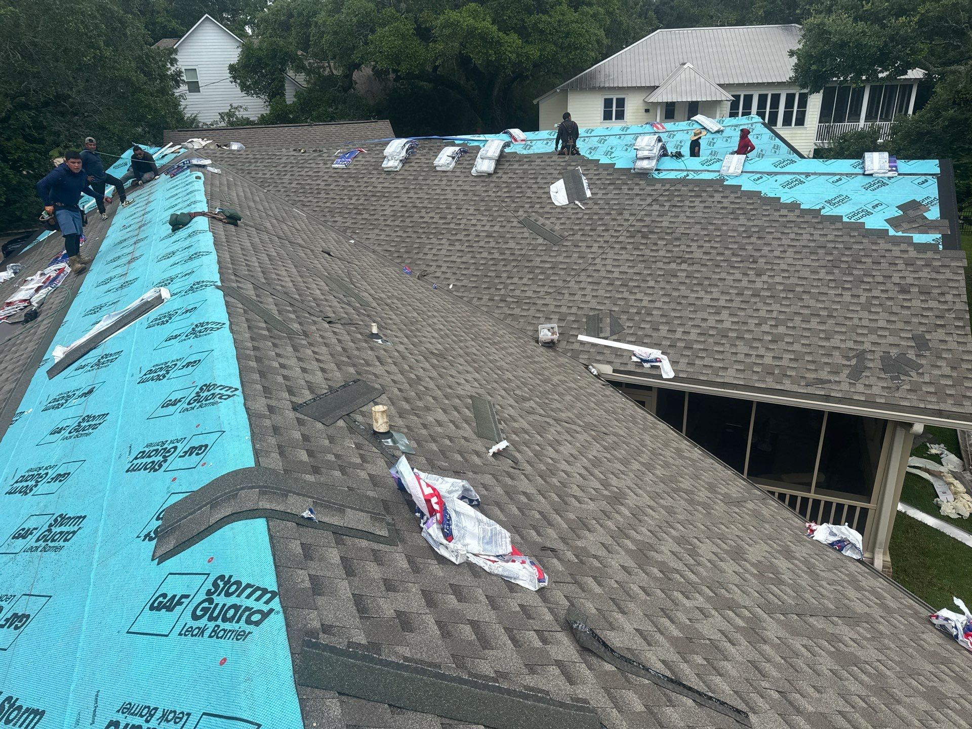 Multiple crew members working both slopes of a large hip roof during a re-roof