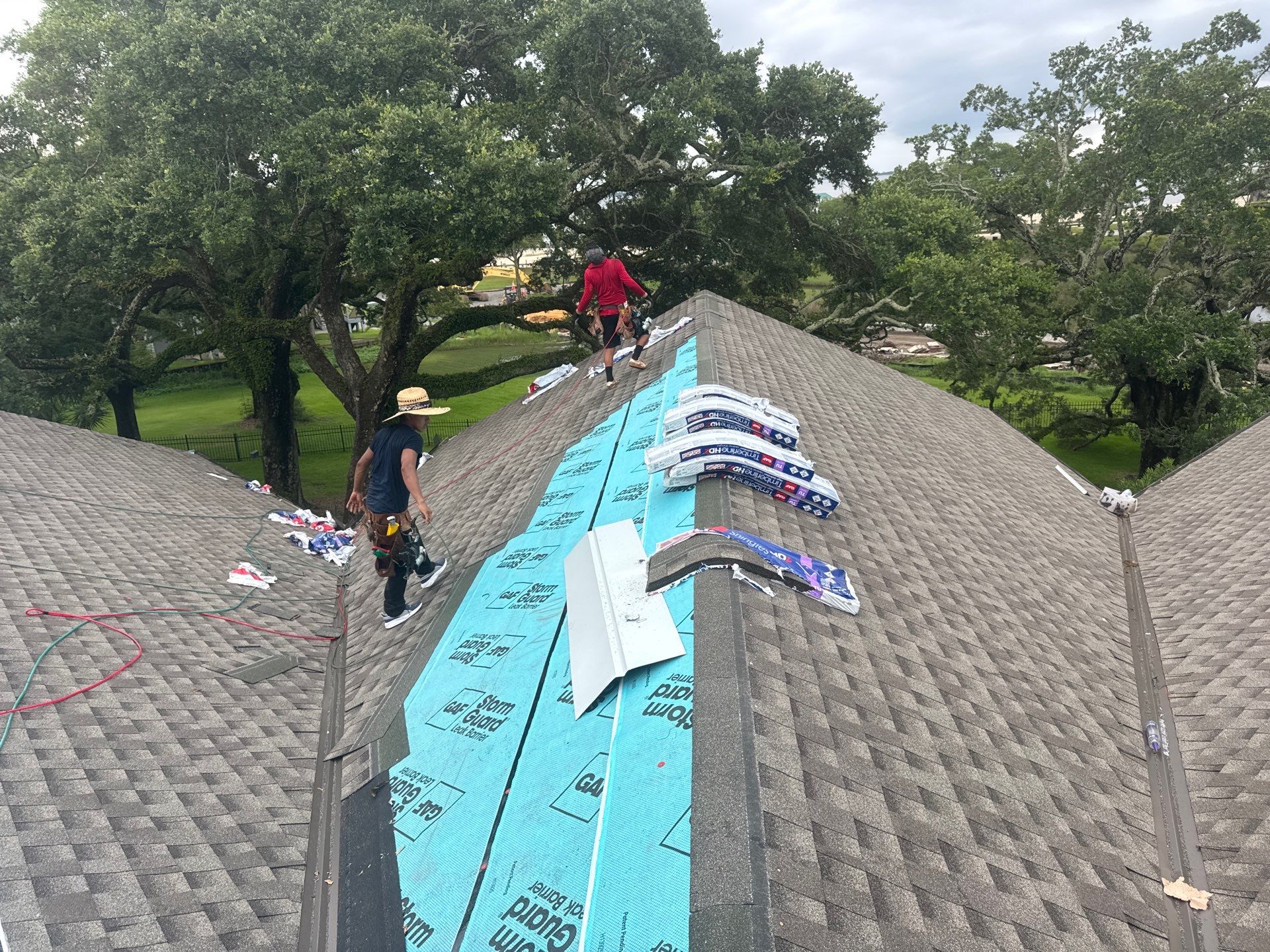 Crew staging GAF Timberline HDZ shingle bundles along the ridge of a steep hip roof