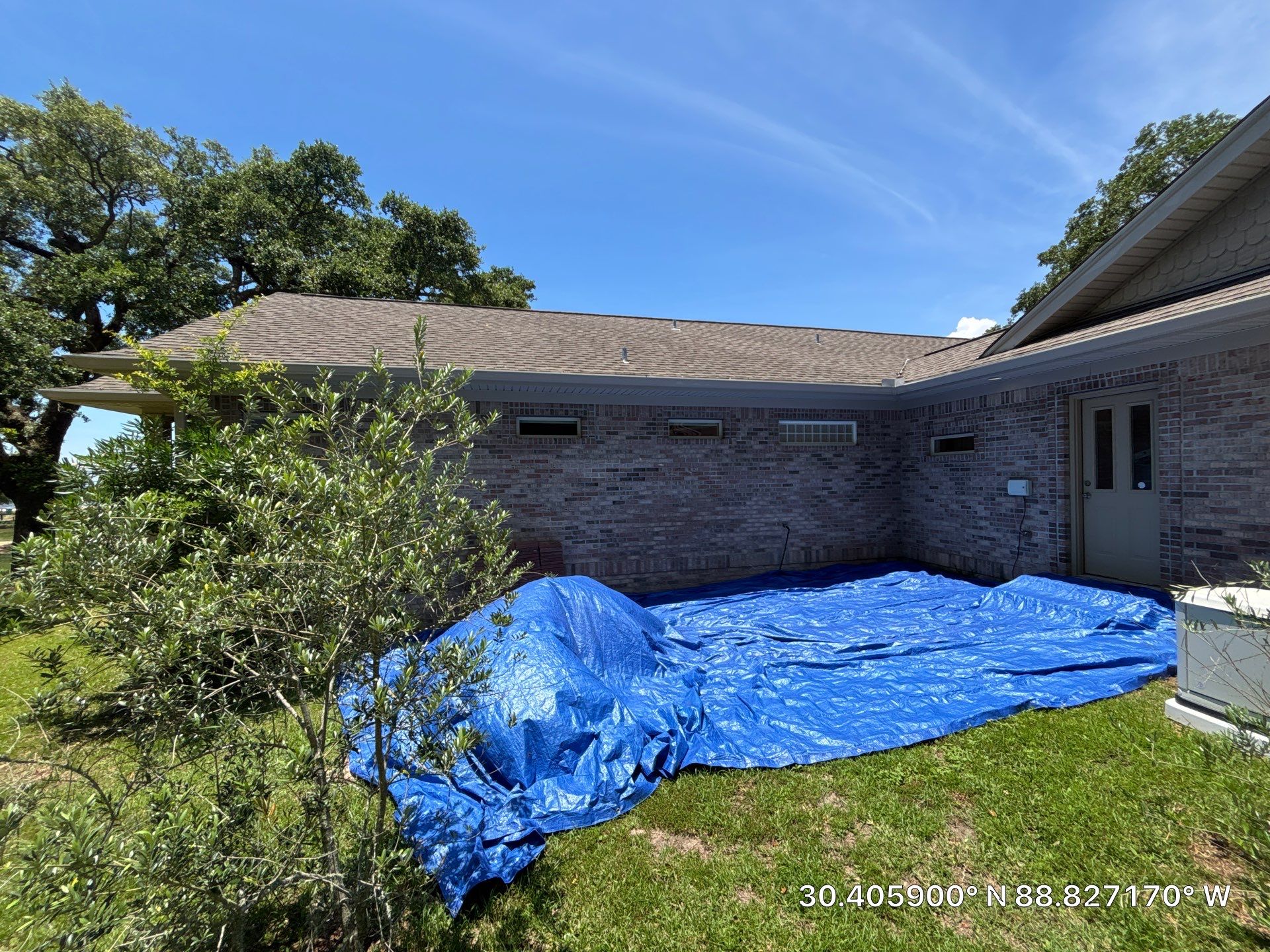 Finished shingle roof with ground tarps protecting landscaping and AC unit