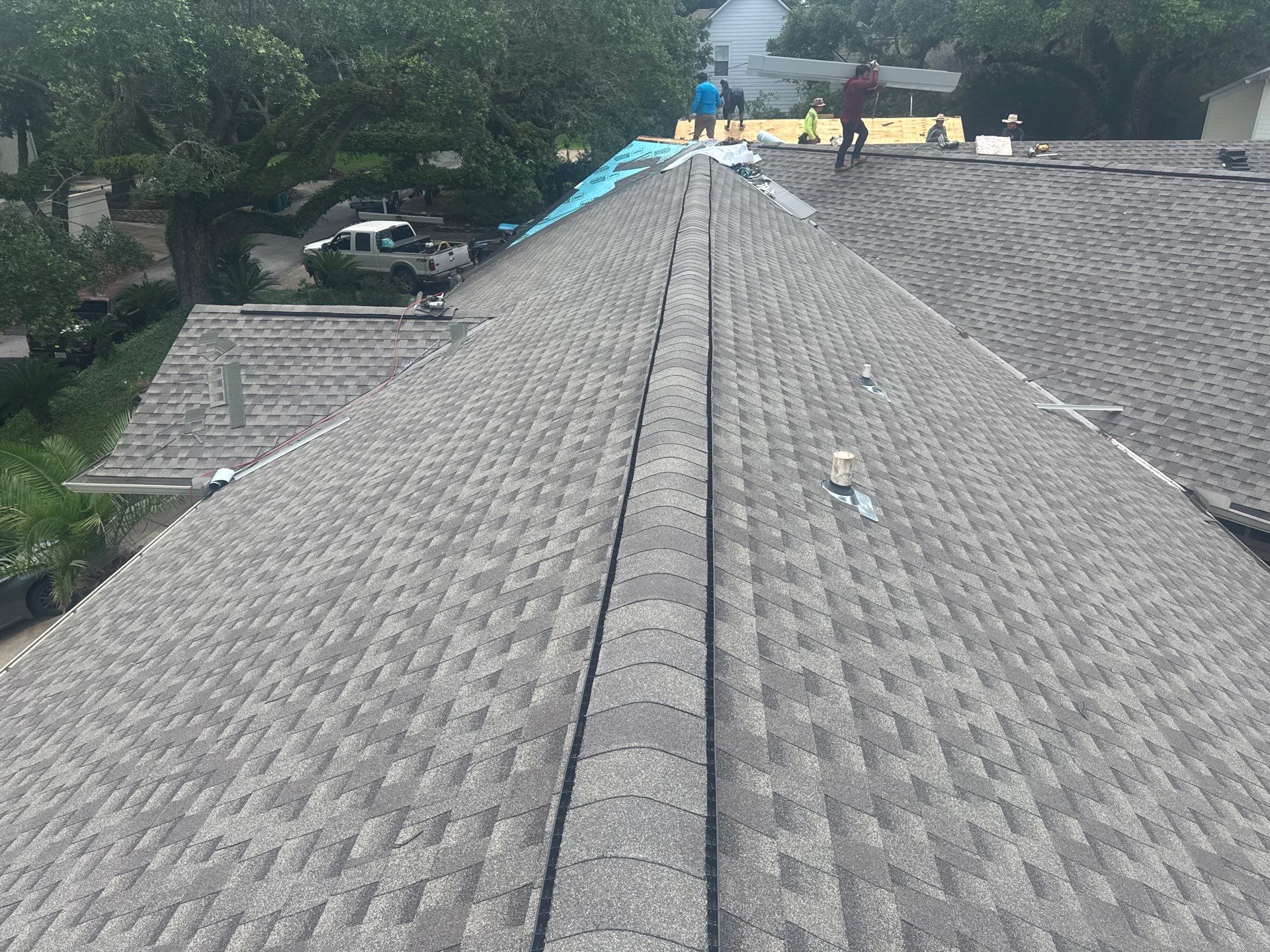 Finished architectural shingle ridge in foreground with crew working tear-off in the background